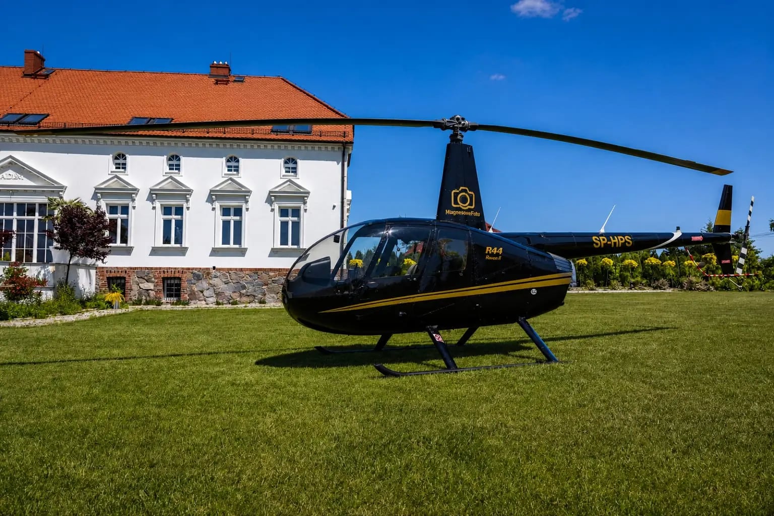 Robinson R44 na trawniku przed białym obiektem weselnym